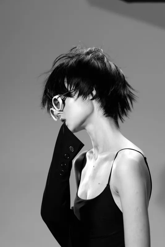 Black and white portrait of a slim woman with short hair wearing sunglasses and a black dress