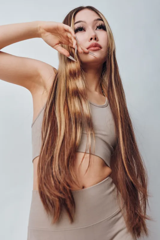 Young woman with long straight hair posing and looking up in beige sportswear top and leggings on white background. Fashion model with smooth hairstyle and natural makeup portrait.