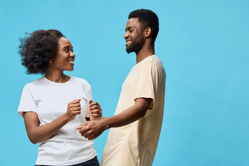 Happy couple dancing together against a bright blue background, showcasing love and joy in modern casual clothing, perfect for relationships and positivity themes