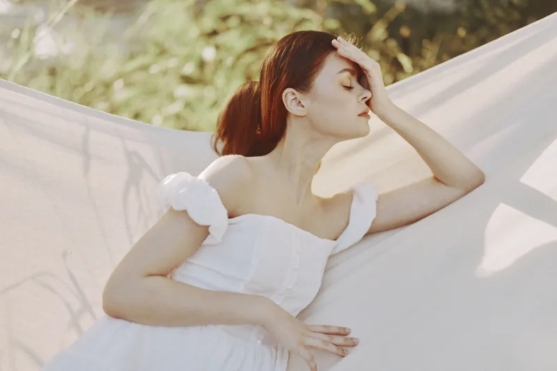 Young woman in a white dress resting outdoors, showcasing tranquility and serenity amidst nature s greenery, embodying relaxation and peace