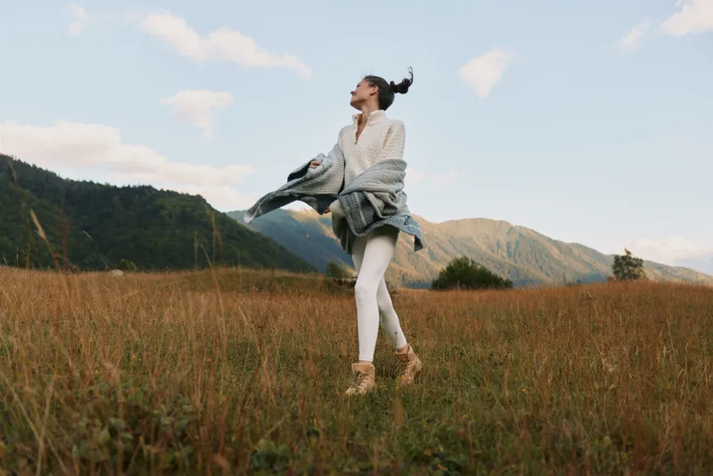 Cheerful woman outdoors in a sunlit field, carefree posture, natural colors, light breeze, relaxed lifestyle moment, joyful smile toward the horizon