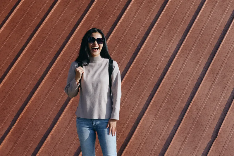 woman, smile, sunglasses, casual, jeans, sweater standing against a striped brick wall with an urban fashion vibe, relaxed pose, street style photography, bright mood