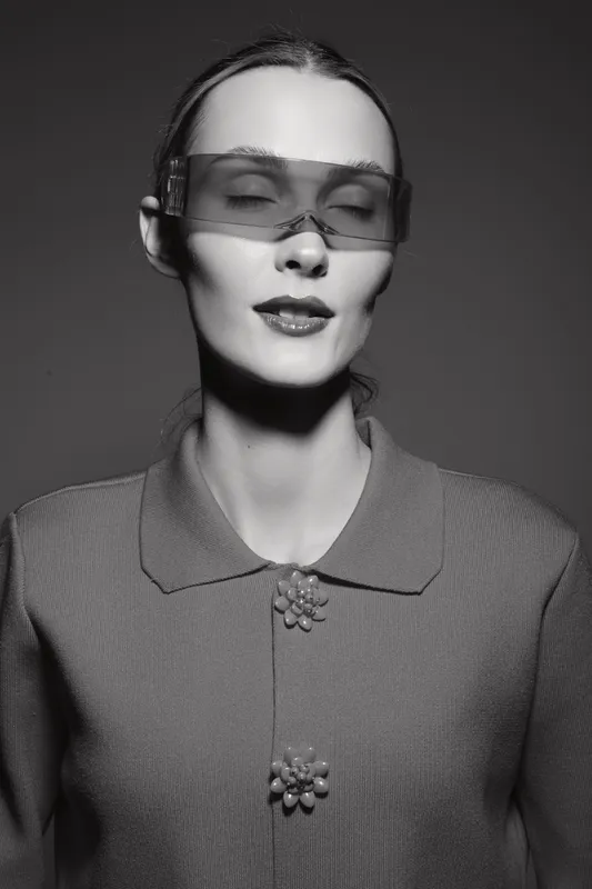 Portrait of a pale white woman with slicked-back hair wearing translucent sunglasses and a textured knit top with floral buttons. Concept of fashion, style, and modern elegance.
