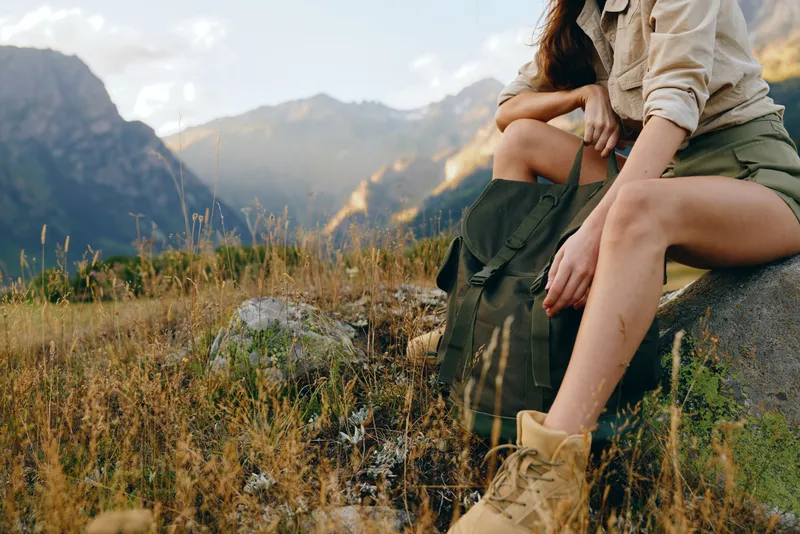 Cheerful woman outdoors, enjoying mountain nature in a casual hiking scene, sitting on a rock, sunlit landscape, relaxed posture, warm colors and natural textures soft