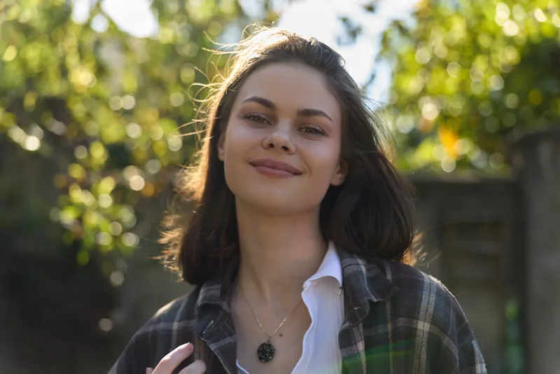 Smiling woman outdoors in daylight wearing casual outfit, enjoying a sunny lifestyle portrait with natural light, portraying relaxed everyday mood and approachable style
