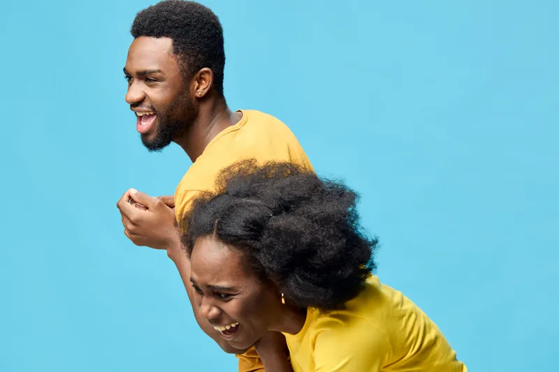 Joyful young African couple laughing together against a bright blue background, wearing matching yellow shirts, embodying happiness and connection