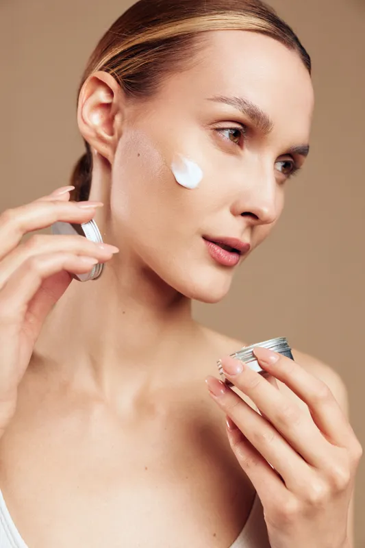 Skincare focused moment with a woman applying moisturizer to the face, gentle expression, creamy texture on cheek, natural tones and soft lighting