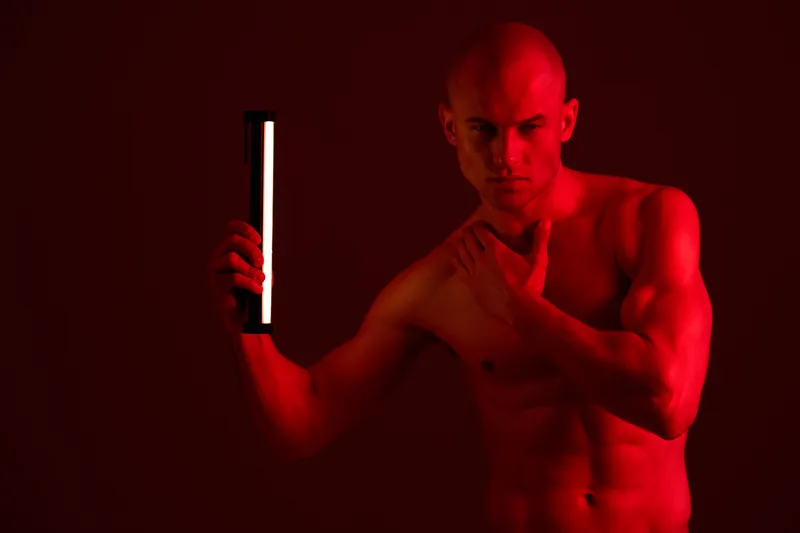 A strong man poses with a light stick in a dramatic red setting, showcasing power and determination in this intriguing black and white style composition.