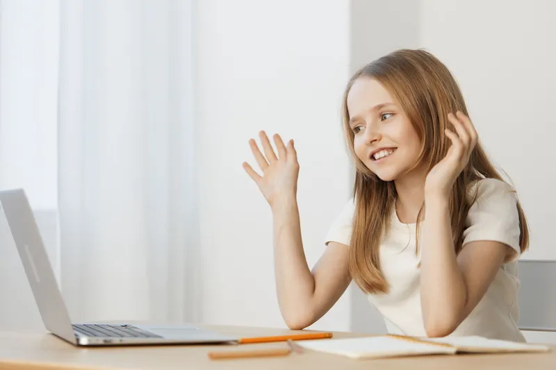 Smiling young girl interacting online with a laptop, showcasing joy and engagement, in a bright, modern workspace