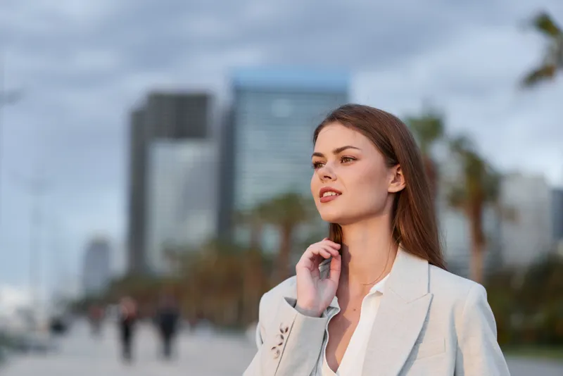 Confident woman in beige blazer outdoors with cityscape background expressing determination and focus in urban business fashion style