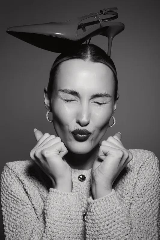 Young white woman with pale skin and dark hair puckers lips with eyes closed and holds fists near face in studio.