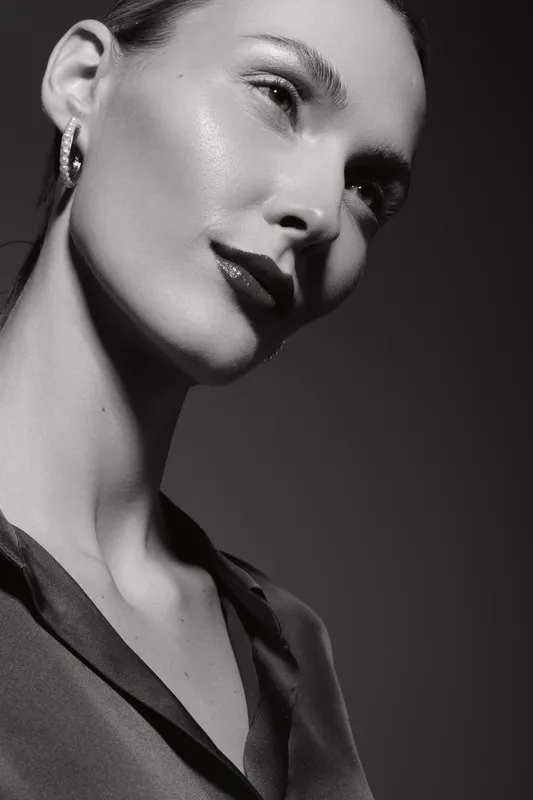Close-up portrait of a fair-skinned Caucasian woman with glossy skin and earrings looking away in soft studio lighting. Concept of beauty and elegance.