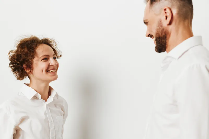 A professional man stands across from a smiling colleague against an isolated colored background, conveying confidence, warmth, and positive emotion in a business scene.