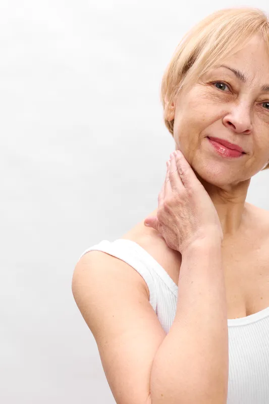Elderly woman portrait for skincare and beauty, she touches her cheek with a gentle smile, focused face, calm wellness, studio white background, aging care and hydration