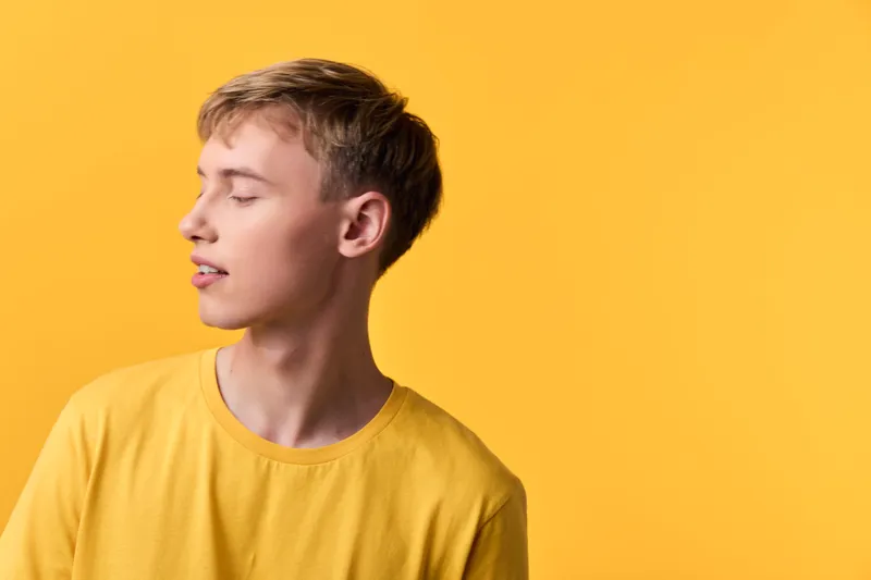 Young man in a yellow shirt turns to the side against a bright yellow background, showcasing a minimalist studio shot with soft lighting and calm mood.