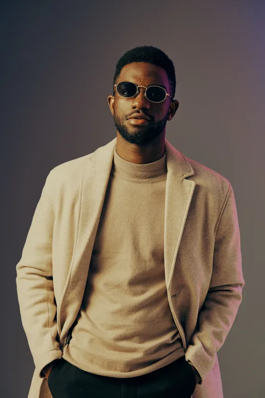 Stylish man in a beige coat and sunglasses, exuding confidence against a gradient background, showcasing modern fashion and urban elegance
