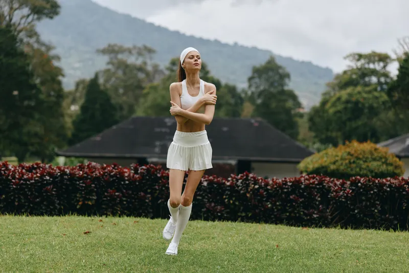 Athletic young woman in white sportswear running outdoors in a beautiful green park, showcasing fitness and vitality with a joyful expression