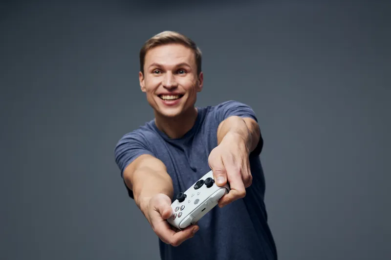 happy man playing video game holding wireless controller smiling casual blue tshirt isolated dark grey background digital entertainment concept