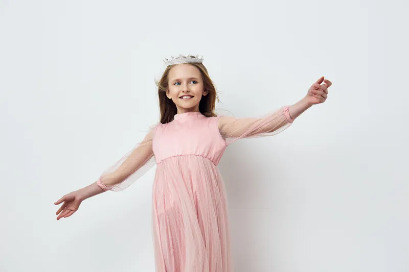 Elegant smiling girl in a pink dress with a crown, joyful expression, minimalist background showcasing youthful beauty and innocence