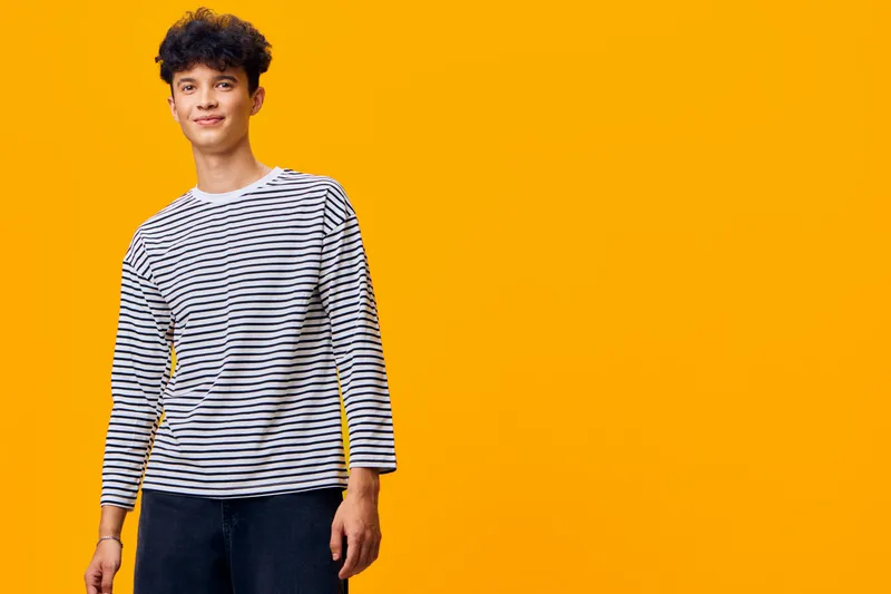 young man with curly hair wearing striped shirt standing confidently against bright yellow background, casual style and relaxed expression