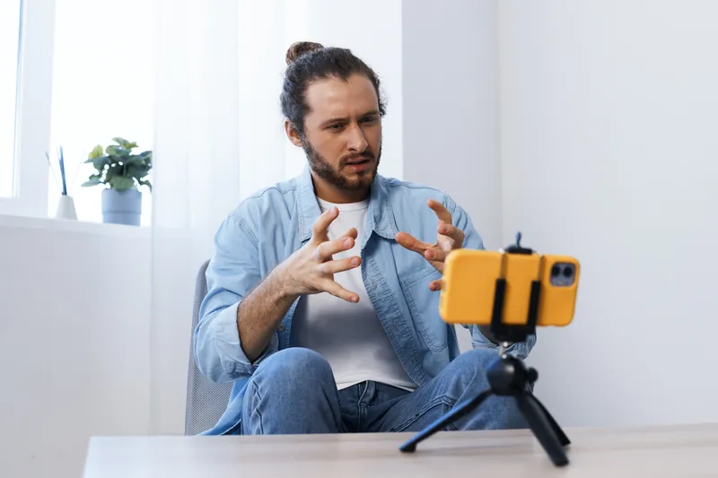 Young man in casual attire expressing emotions while communicating on a smartphone, showcasing a relaxed environment with bright colors