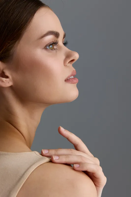 Beauty woman profile with flawless skin, soft makeup, and natural light on a neutral gray background, showcasing elegance and grace in a minimalist fashion style.