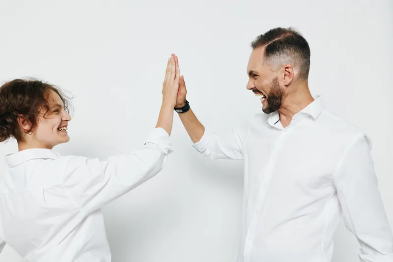 A confident business professional man and a colleague celebrate success with a high five on an isolated colored background, showcasing teamwork, emotion, and professional energy.