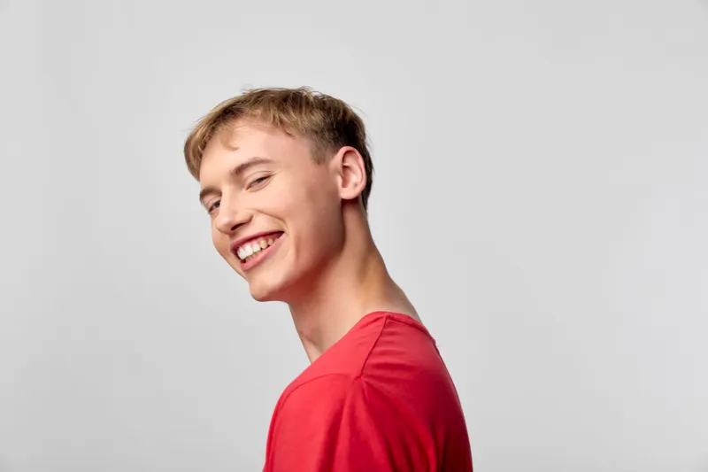 Smiling young man in a red shirt stands in a bright studio, radiating happiness and friendly energy, casual lifestyle shot suitable for branding, social campaigns and positive messaging