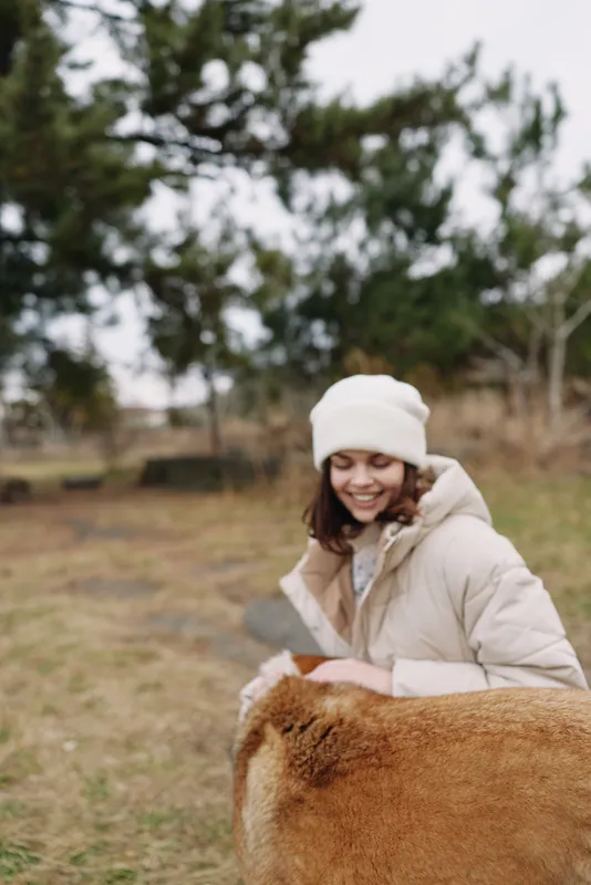 Woman in a winter coat and beanie interacts with a calm cow in a field, an outdoor pasture scene showing gentle animal care and rural life