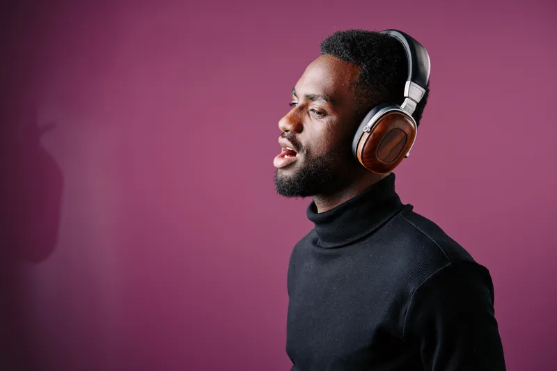 A young African man wearing headphones, singing passionately against a purple background, showcasing emotion and modern style in portrait photography