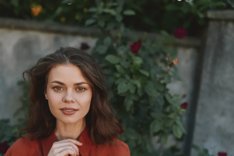 A woman in a red blouse stands outdoors, relaxed pose, soft natural light. A calm lifestyle portrait exploring everyday confidence, gentleness, and selfassurance