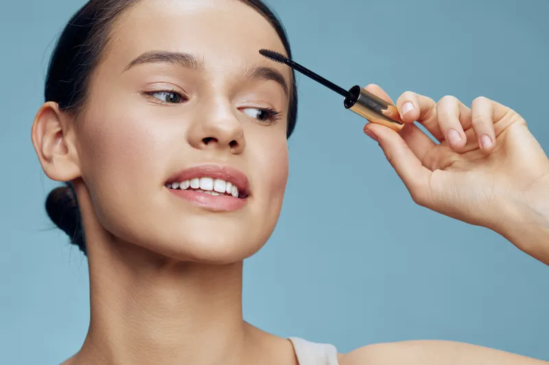 Portrait of a young woman applying mascara in a minimalist setting, showcasing beauty and confidence with soft features and a serene expression