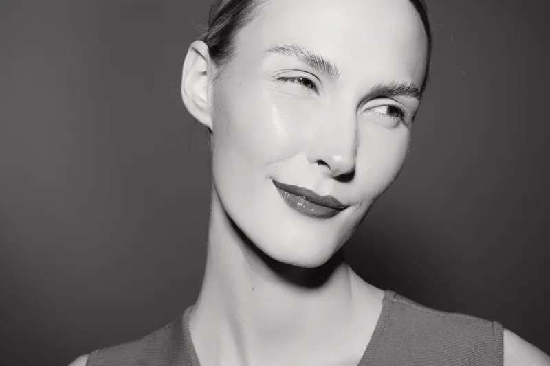 Close-up portrait of young white woman with pale skin and red lips smiling, looking aside on dark background. Concept for beauty and natural expression.