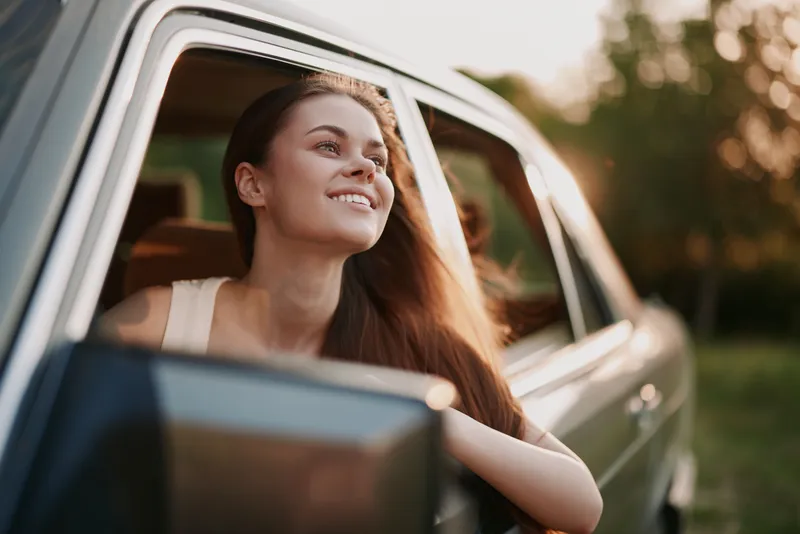 Young woman enjoying a sunny day driving with her hair flowing in the breeze, capturing joy and freedom in a vintage car setting.