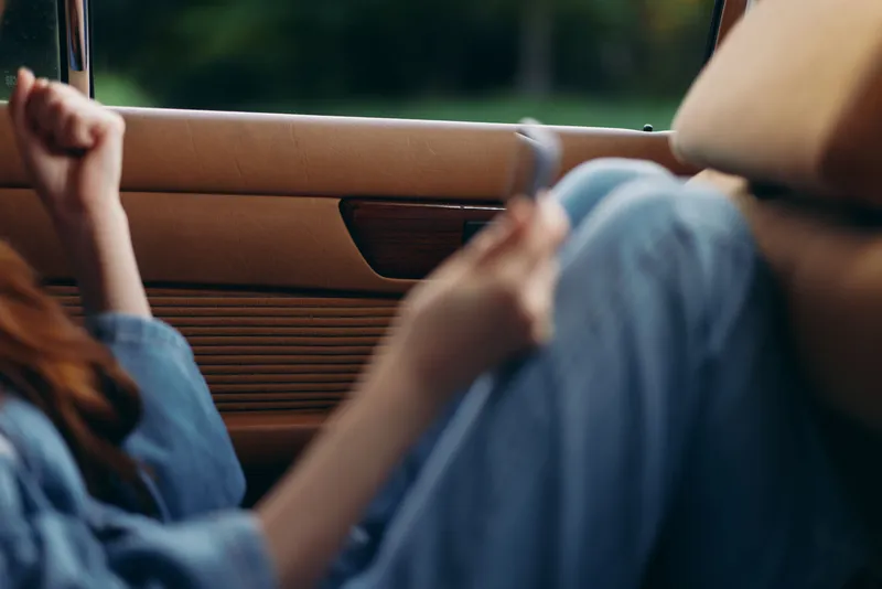 Relaxed young woman enjoying leisure time in a vintage car, dressed in denim, with a joyful expression, embodying carefree summer vibes and a sense of freedom.