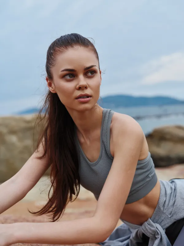 Young woman in sporty attire exercising outdoors by the beach, showcasing a healthy lifestyle, natural beauty, and emotional focus on fitness