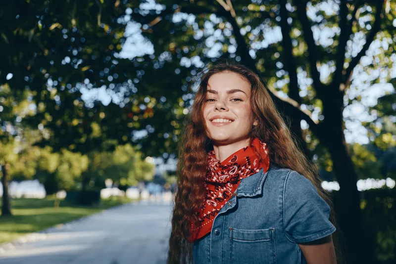 lifestyle woman in modern boho-western denim street style wearing red bandana outdoors with natural light and film color effect, smiling confidently