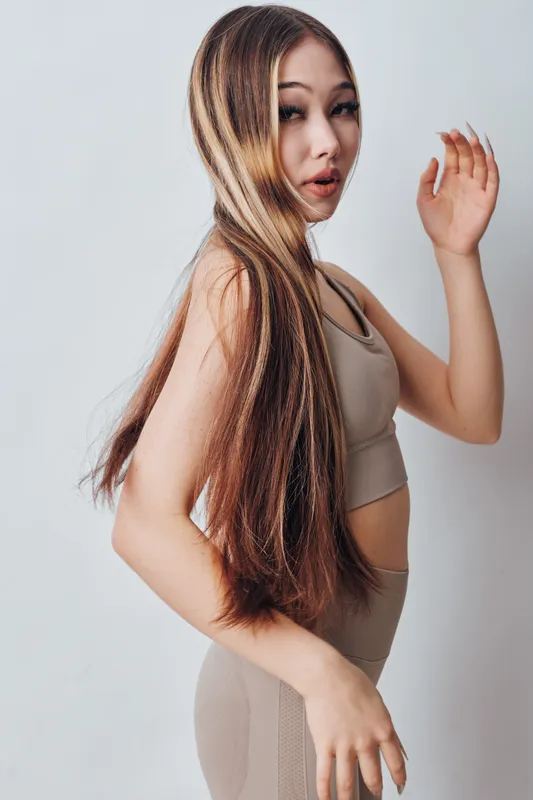 Woman with long shiny hair wearing beige sportswear posing on gray background showing hairstyle and makeup in studio for beauty and fashion concept.