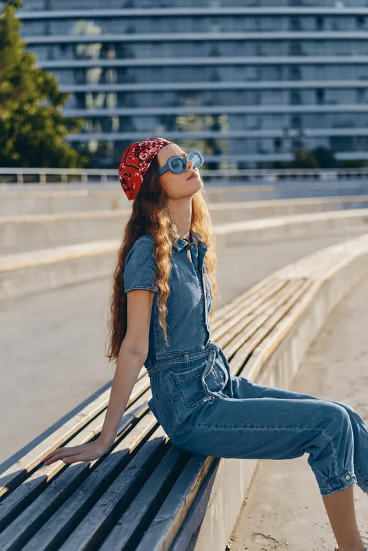 Lifestyle woman in modern boho-western denim street style with long hair and red bandana, enjoying sunny urban outdoors with film color warmth and relaxed attitude.