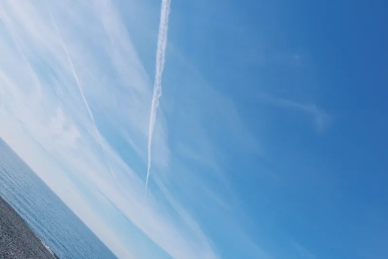 Sky, ocean and contrail composition with blue tones and distant horizon, featuring clear weather, calm water and a jet trail for travel, exploration and wide open space.