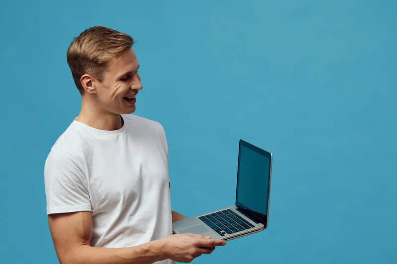 smiling man holding laptop working digital nomad casual white t-shirt blue background technology concept remote work