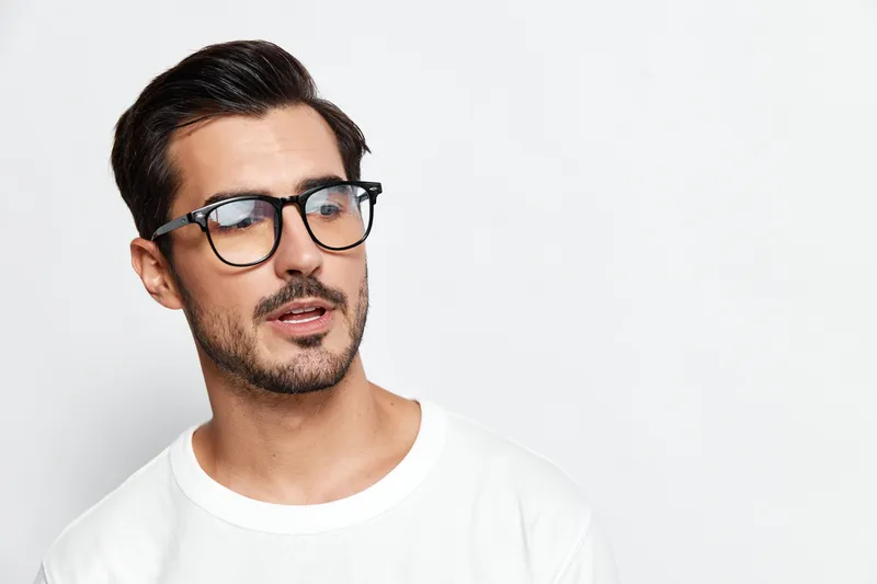 Stylish young man wearing glasses, looking thoughtfully at the camera with a serious expression, isolated on a plain solid background. People lifestyle concept.