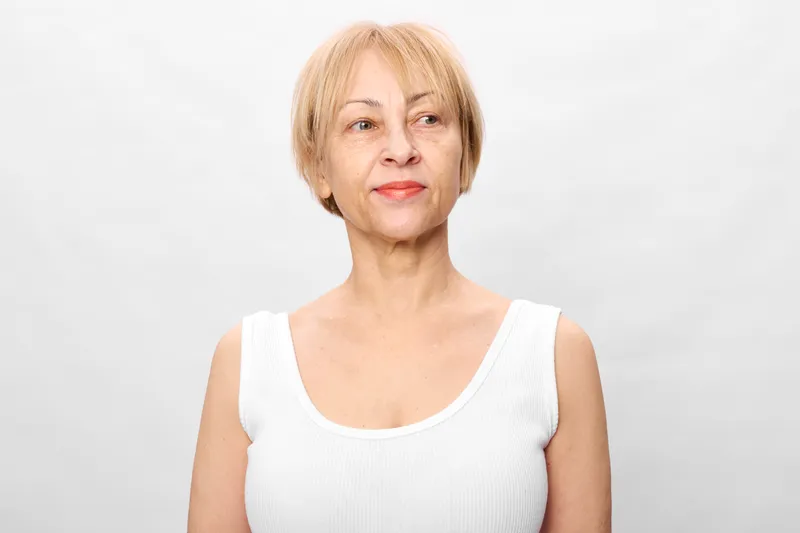 Elderly woman senior portrait, calm neutral expression, confidence in studio light, white background, soft focus, shoulders visible, concept for aging and wellness in healthcare