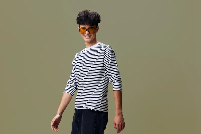 smiling man wearing striped shirt and orange sunglasses stands against plain background, casual style and modern hair, bright mood and youthful appearance