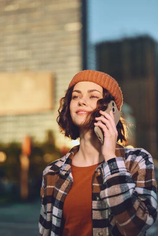 woman phone smile urban golden beanie plaid candid portrait of a young millennial enjoying city sunlight with authenticity, candid lifestyle, golden hour glow, mindful living and emotional