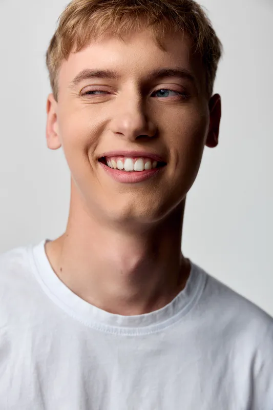 Smiling man in a white tshirt with a friendly expression, close up shot, showing warmth and confidence. Clean studio lighting highlights a natural, relaxed mood, ideal for uplifting lifestyle or