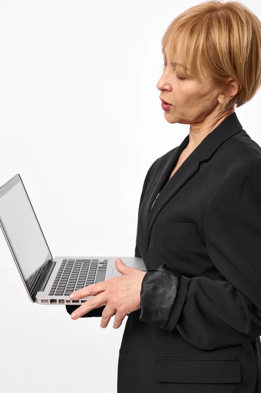 Businesswoman senior typing on laptop in corporate office, technology concept, clean background, focused side view, professional suit, isolated, white backdrop