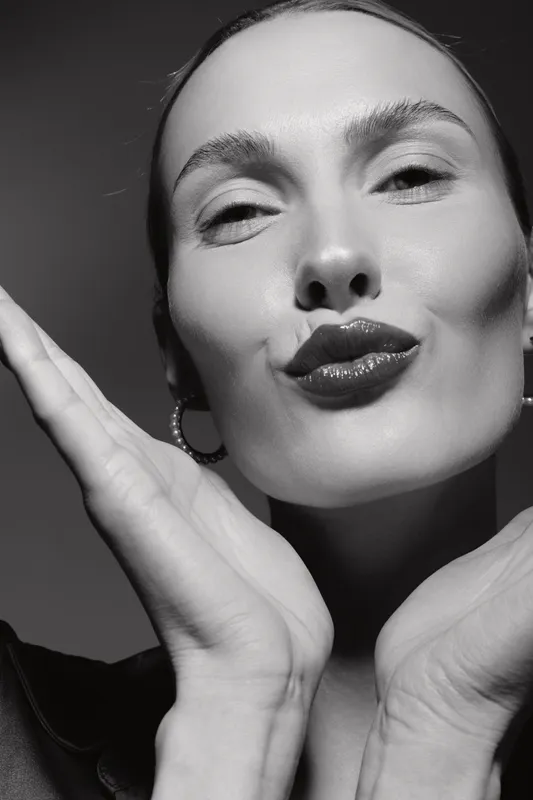 Close-up of a fair skinned white woman with slicked hair sending a kiss, wearing hoop earrings in a black and white portrait.