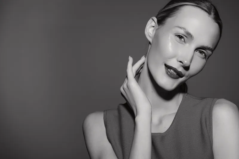 Portrait of a smiling Caucasian woman with fair skin and slicked back hair in monochrome studio. Concept for beauty, skincare, and elegance.