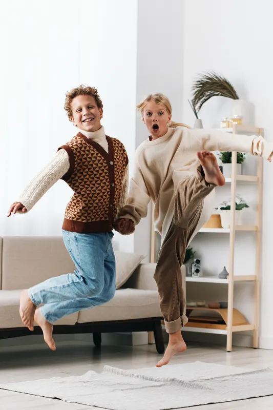 Authentic playful moment with children in a cozy home, school style outfits, and spontaneous jump energy capturing joy, movement, and everyday life.